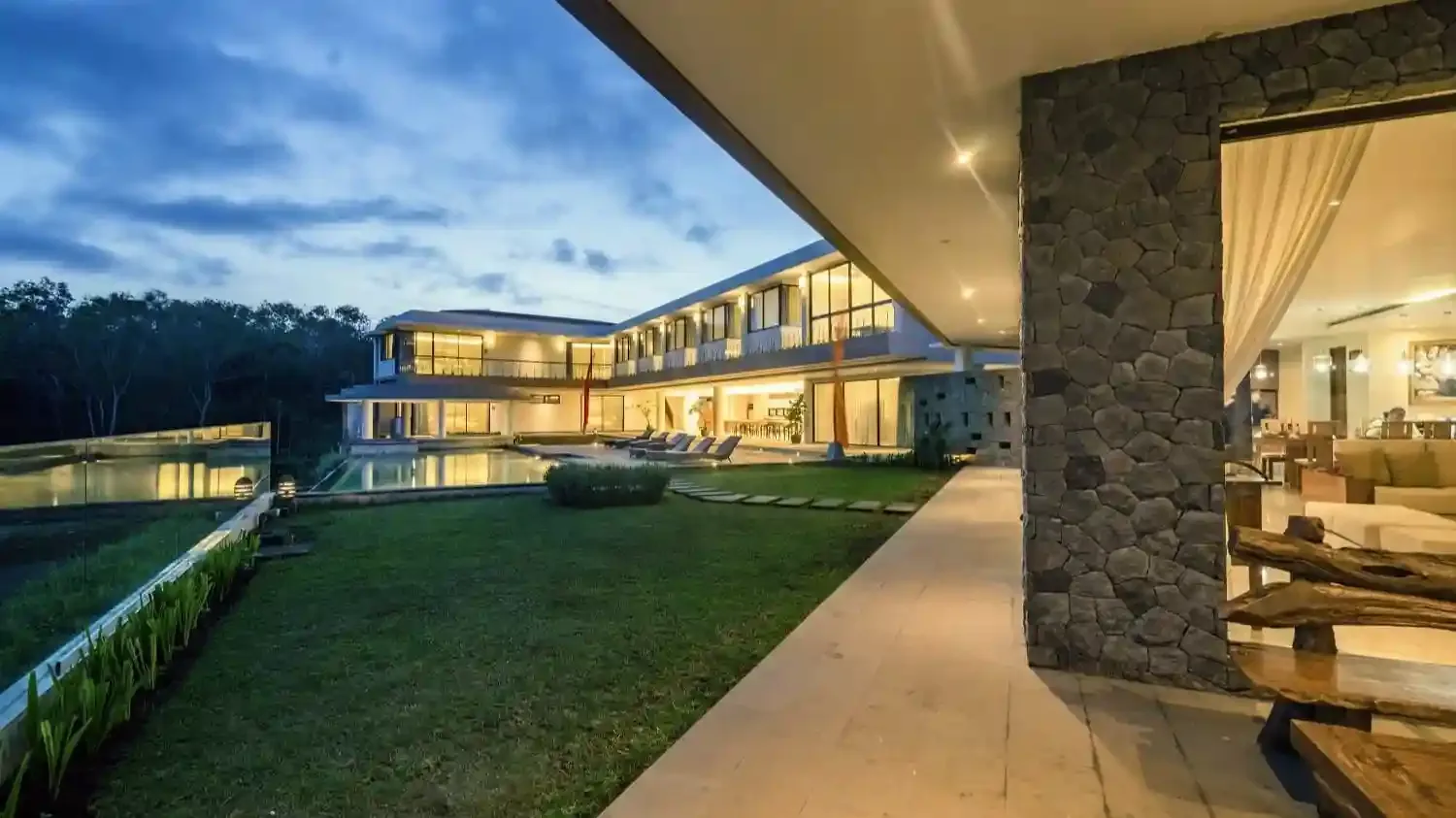 Uluwatu villa building at dusk with lit interiors overlooking a lawn
